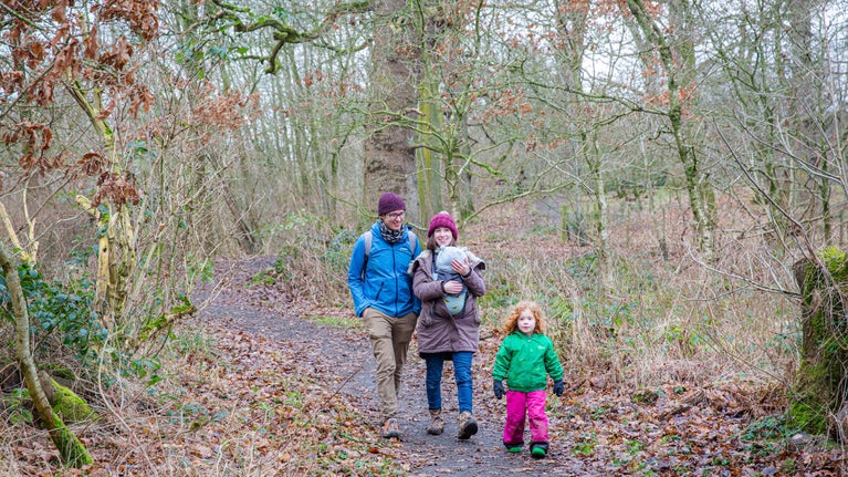 A family walking through woodland in winter at Acorn Bank, Cumbria